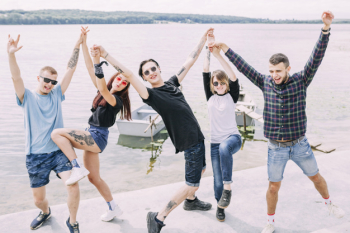 Group of happy carefree friends dancing near lake
