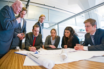 Group of seven designers discussing blueprints in a conference room.