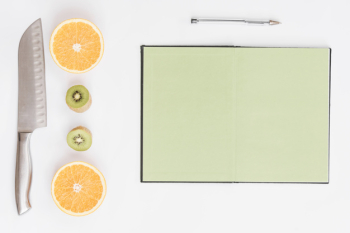 Halved oranges; kiwi; knife; pen and blank page notebook on white background