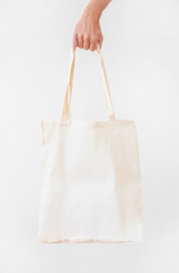 Hand holding blank white fabric canvas bag isolated over white background