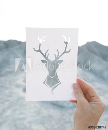 Hand holding perforated paper moose art with mountain background