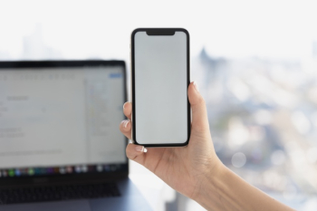 Hand holding phone in front of laptop mock-up Free Photo