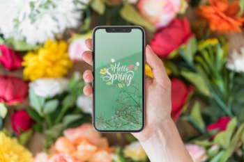 Hand holding smartphone mockup above flowers Free Psd