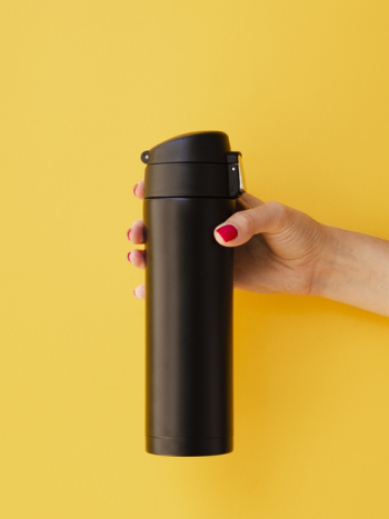 Hand holding thermos mock-up on yellow background Free Photo