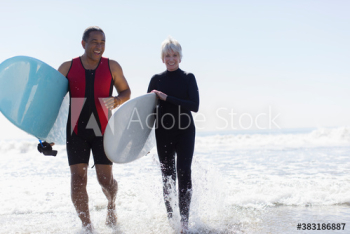 Happy active senior couple with surfboards running in ocean surf