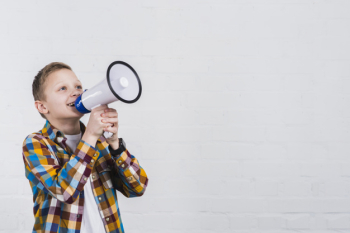 Happy boy shouting through megaphone standing against white wall