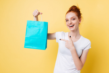 Happy ginger woman holding packet and pointing at him Free Photo