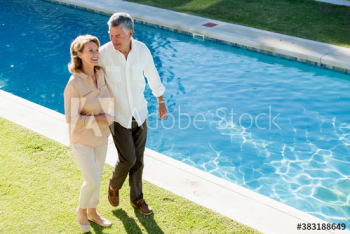 Happy senior couple walking along sunny swimming pool Happy senior couple walking along sunny swimming pool