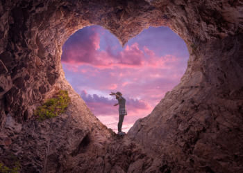 Happy woman enjoying in idyllic mountain nature, celebrating freedom and rising her arms while standing toward the setting sun. Valentines day concept.
