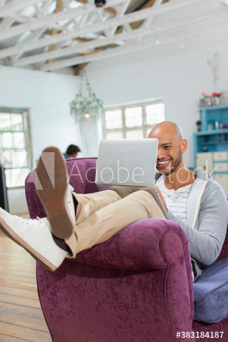 Happy young man using laptop in armchair Happy young man using laptop in armchair
