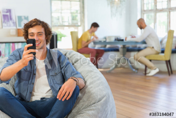 Happy young man using smart phone in beanbag chair Happy young man using smart phone in beanbag chair