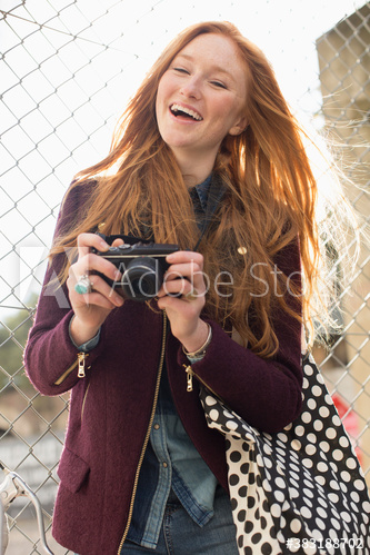 Happy young woman with camera at chainlink fence Happy young woman with camera at chainlink fence