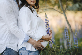 Husband hugs for back his pregnant wife among lupins field, close up Free Photo