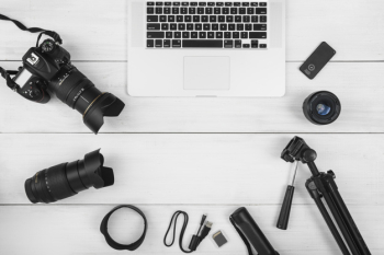 Laptop surrounded with camera accessories on white wooden desk
