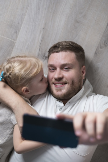 Little girl kissing father while taking selfie Free Photo