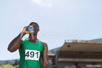 Male track and field athlete drinking sports drink on sunny field Male track and field athlete drinking sports drink on sunny field