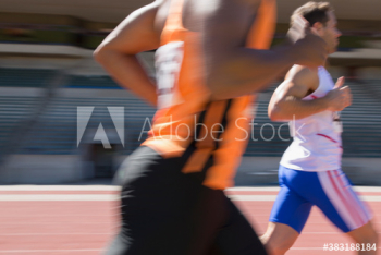 Male track and field athletes racing on sunny running track Male track and field athletes racing on sunny running track