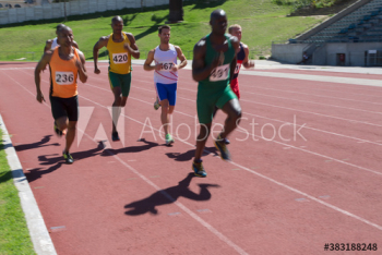 Male track and field athletes racing on sunny running track Male track and field athletes racing on sunny running track