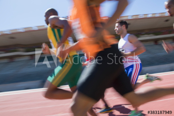 Male track and field athletes racing on sunny sports track Male track and field athletes racing on sunny sports track
