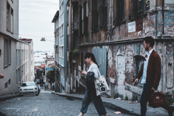 Man and Woman Crossing A City Street With An Old Abandoned Building In The Corner