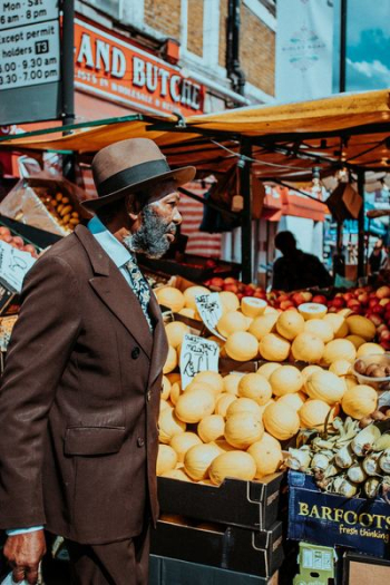 man in brown blazer standing on front of fruit displays near building