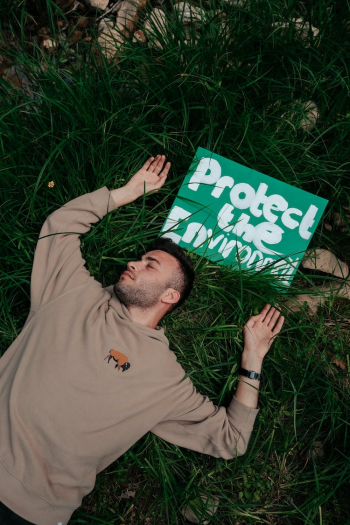 Man in Brown Long Sleeve Shirt Lying on Green Grass with a Sign Above His Head