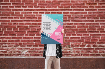 Man presenting poster mockup in front of brick wall Free Psd