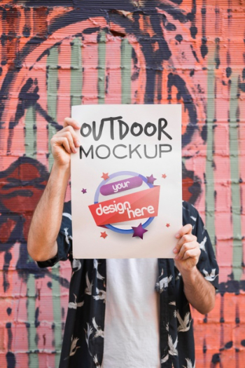 Man presenting poster mockup in front of graffiti wall Free Psd