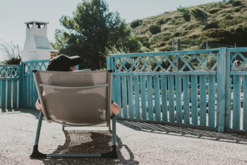 Man Sitting on Lounger Near Blue Wooden Fence Man Sitting on Lounger Near Blue Wooden Fence
