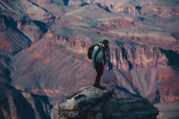 man standing on rock cliff overlooking canyon during daytime man standing on rock cliff overlooking canyon during daytime