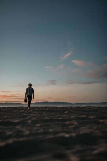 man walking on sand while holding his footwears man walking on sand while holding his footwears