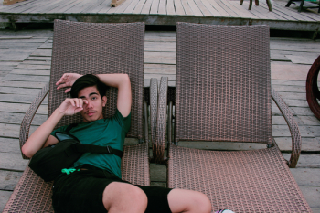 Man Wearing Green Shirt and Black Shorts Laying on Lounger