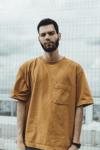 Man Wearing Orange Crew-neck Shirt Standing Besides Gray Metal Fence Man Wearing Orange Crew-neck Shirt Standing Besides Gray Metal Fence