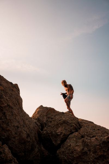 man wearing white shorts standing on brown rocks under clear blue sky