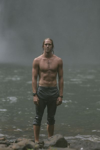 man wears black pants stands on rocks near body of water