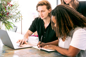 Man Working on Laptop while Woman Takes Notes Man Working on Laptop while Woman Takes Notes