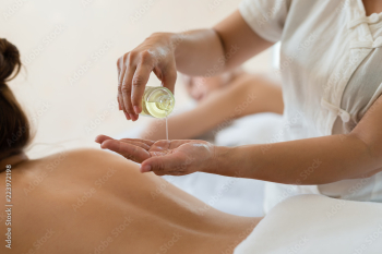 Masseuse pour oil on the hand and young asian woman relaxing receiving back massage at spa salon