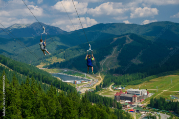 mountain landscape - two tourists fly on a cable on suspensions through a deep abyss against the backdrop of mountain snowy peaks of the Caucasus Mountains