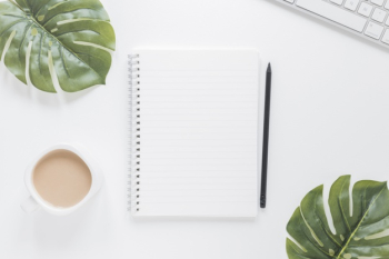 Notebook near coffee cup and keyboard on table with green leaves Free Photo