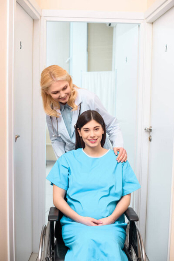 Obstetrician gynecologist riding pregnant woman on wheelchair at maternity hospital and supporting her