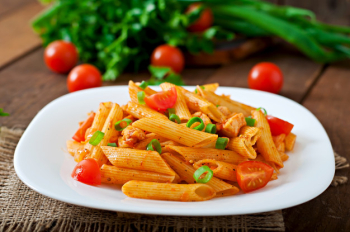 Penne pasta in tomato sauce with chicken and tomatoes on a wooden table Free Photo