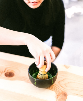 Person Holding a Bamboo Whisk in a Black Bowl Close-up Photography Person Holding a Bamboo Whisk in a Black Bowl Close-up Photography