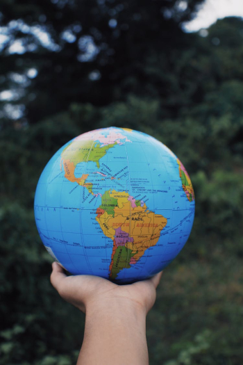 Person holding Earth globe in hand against green trees