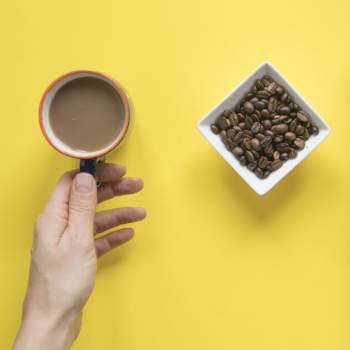 Person's hand taking coffee cup with roasted coffee beans on yellow background