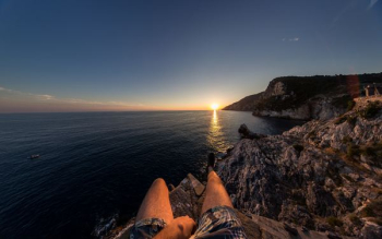 person sitting on cliff in front of sea person sitting on cliff in front of sea