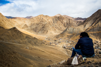 Person Sitting on Mountain Under White Sky Person Sitting on Mountain Under White Sky