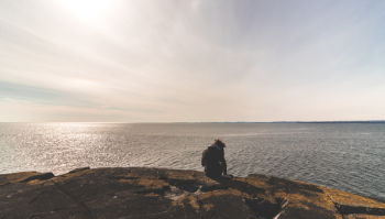 Person Sitting on Stone in Front of Sea Water Person Sitting on Stone in Front of Sea Water