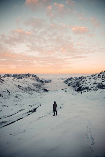 Person Standing in Snowy Field Under White and Orange Skies Person Standing in Snowy Field Under White and Orange Skies