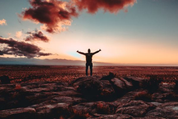 person standing on rock raising both hands person standing on rock raising both hands