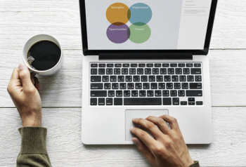 Person Using Macbook Pro While Holding Ceramic Mug on Gray Wood Surface